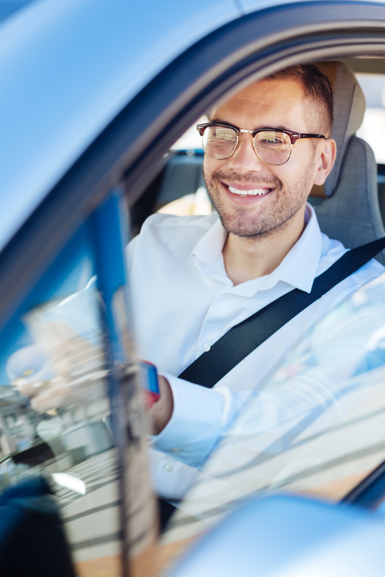 Man with glasses in the drivers seat of a car smiling